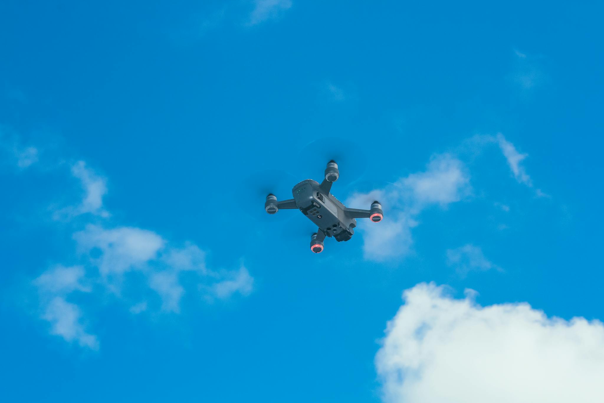 From below of bottom part of quadcopter with propellers and camera for taking photo and video in blue sky with clouds