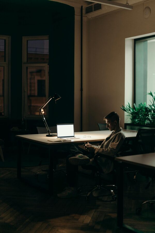 Man in Black and White Plaid Dress Shirt Sitting on Chair in Front of Macbook